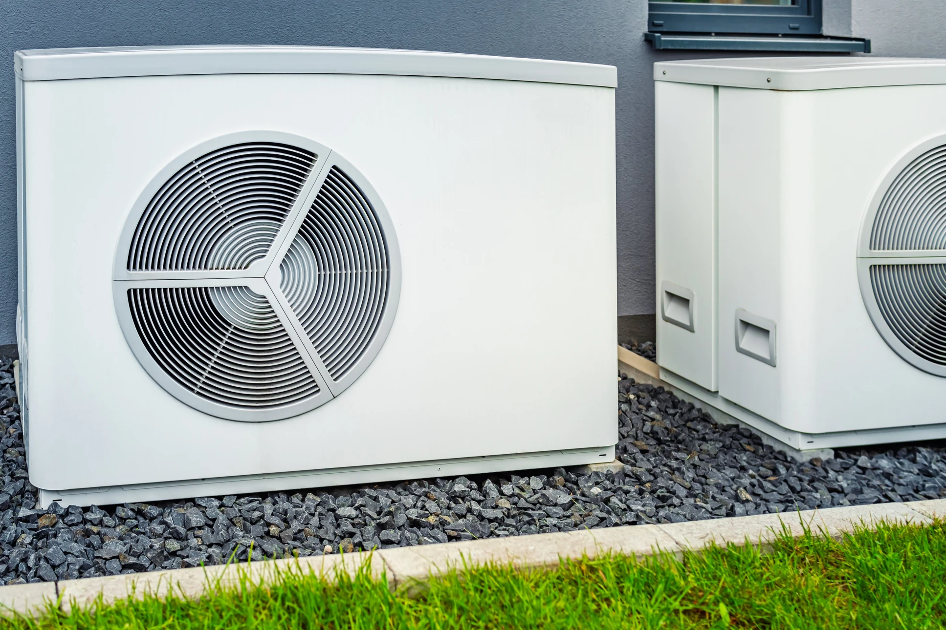 Extérieur résidentiel avec deux pompes à chaleur air-eau installées sur lit de gravier, bordure d'herbe visible
