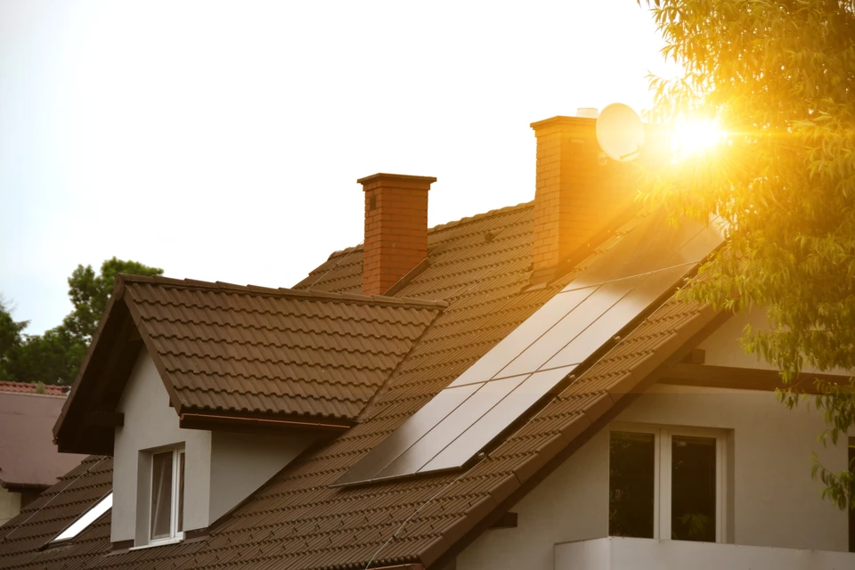 Maison résidentielle avec panneaux solaires photovoltaïques installés sur toiture en tuiles, éclairée par soleil couchant