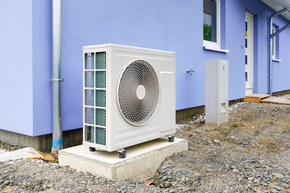 Extérieur résidentiel avec unité de climatisation installée sur dalle béton devant maison bleue
