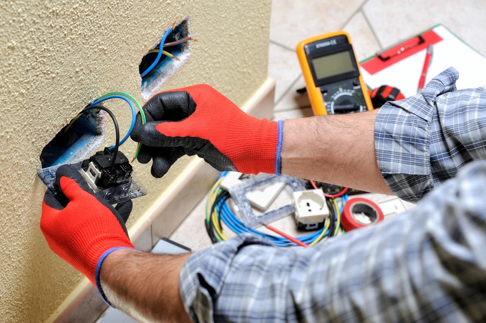 Électricien professionnel travaillant sur installation électrique résidentielle, manipulant multimètre et câblage dans boîtier mural