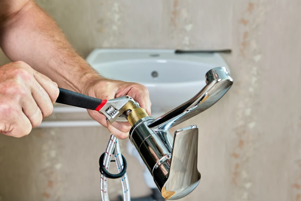 Plombier effectuant la réparation d'un robinet de salle de bain, utilisant une clé à molette pour dévisser les raccords