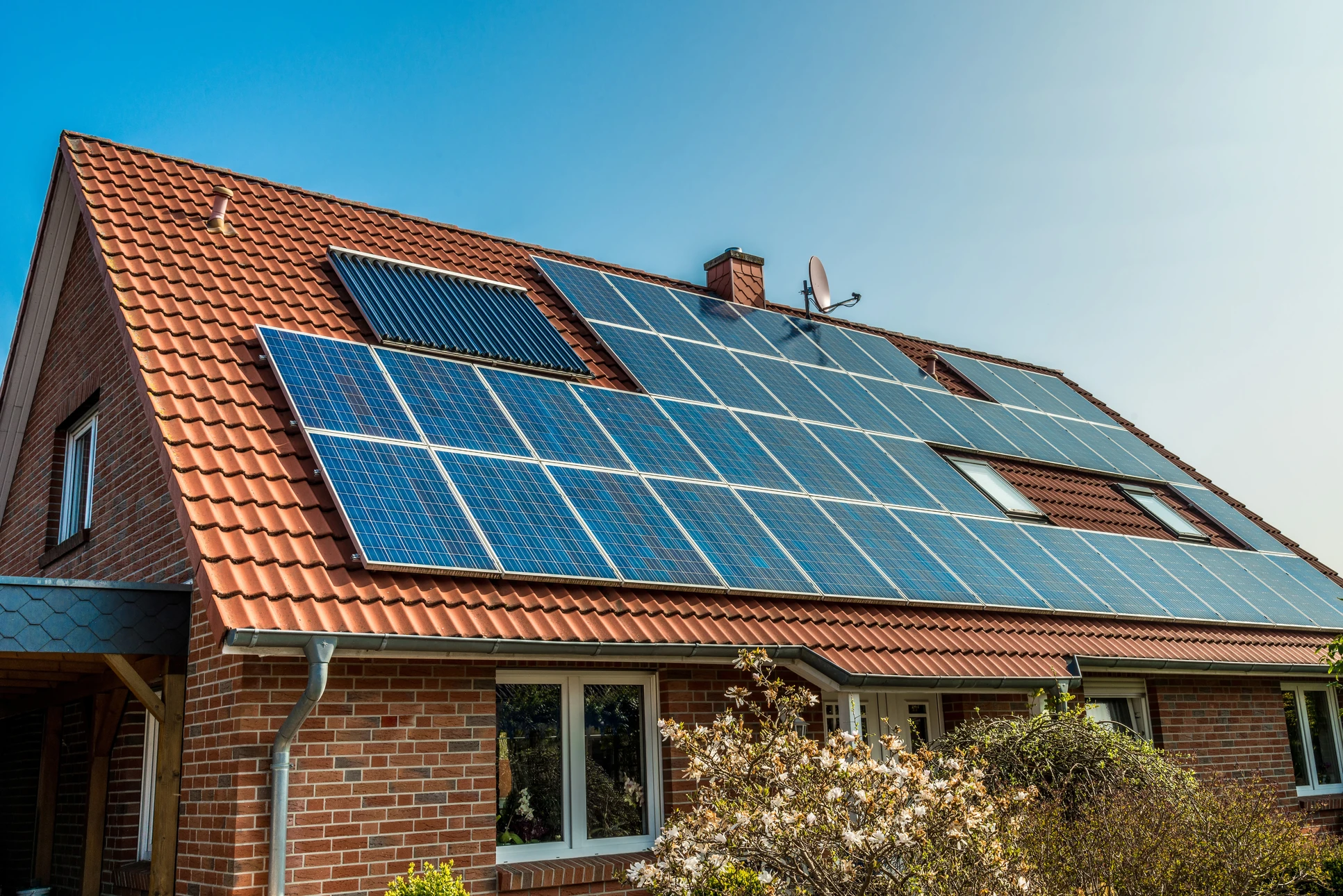 Maison résidentielle en briques avec toiture en tuiles rouges équipée de panneaux solaires photovoltaïques et capteurs solaires thermiques