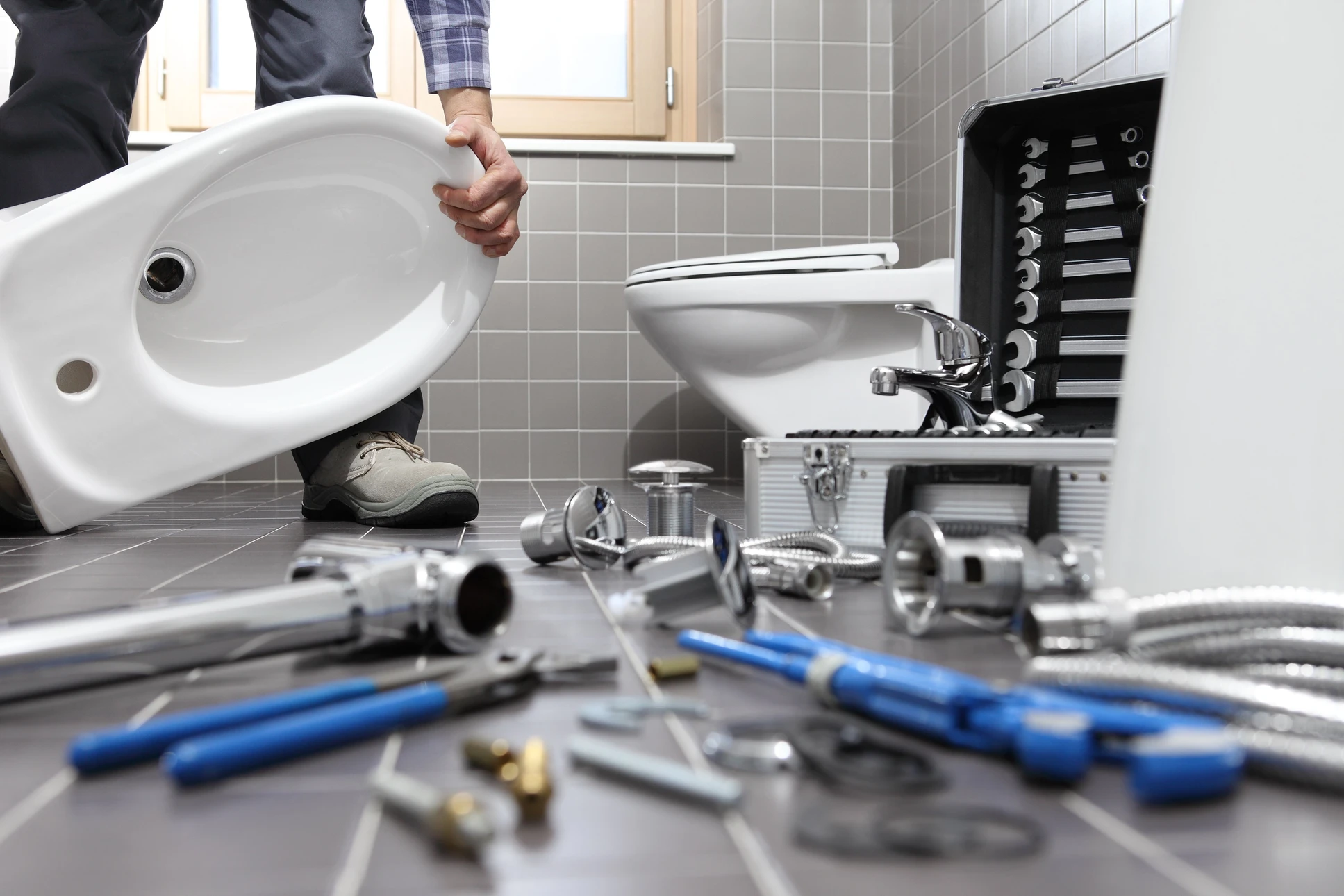 Intérieur salle de bain carrelée grise, plombier installant un lavabo blanc suspendu